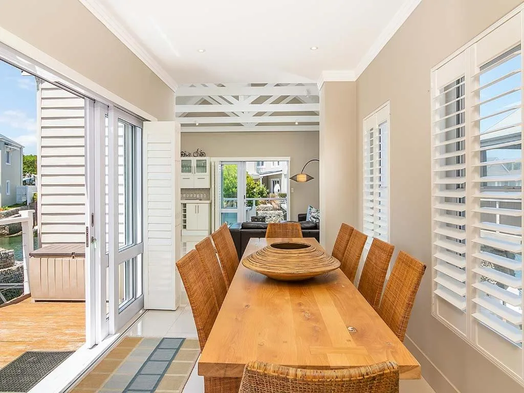 Spacious dining room with wooden table and woven chairs, bright shutters