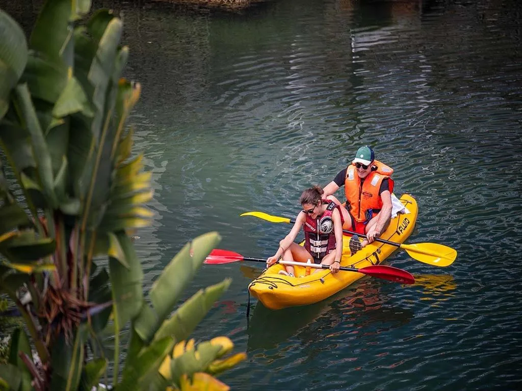 Two people kayaking on calm lagoon water with lush vegetation framing the scenic waterway