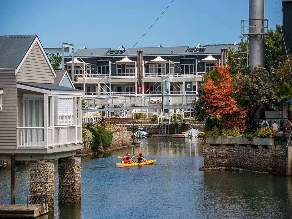 Waterfront canal view with kayakers, colorful autumn trees, and modern waterfront properties