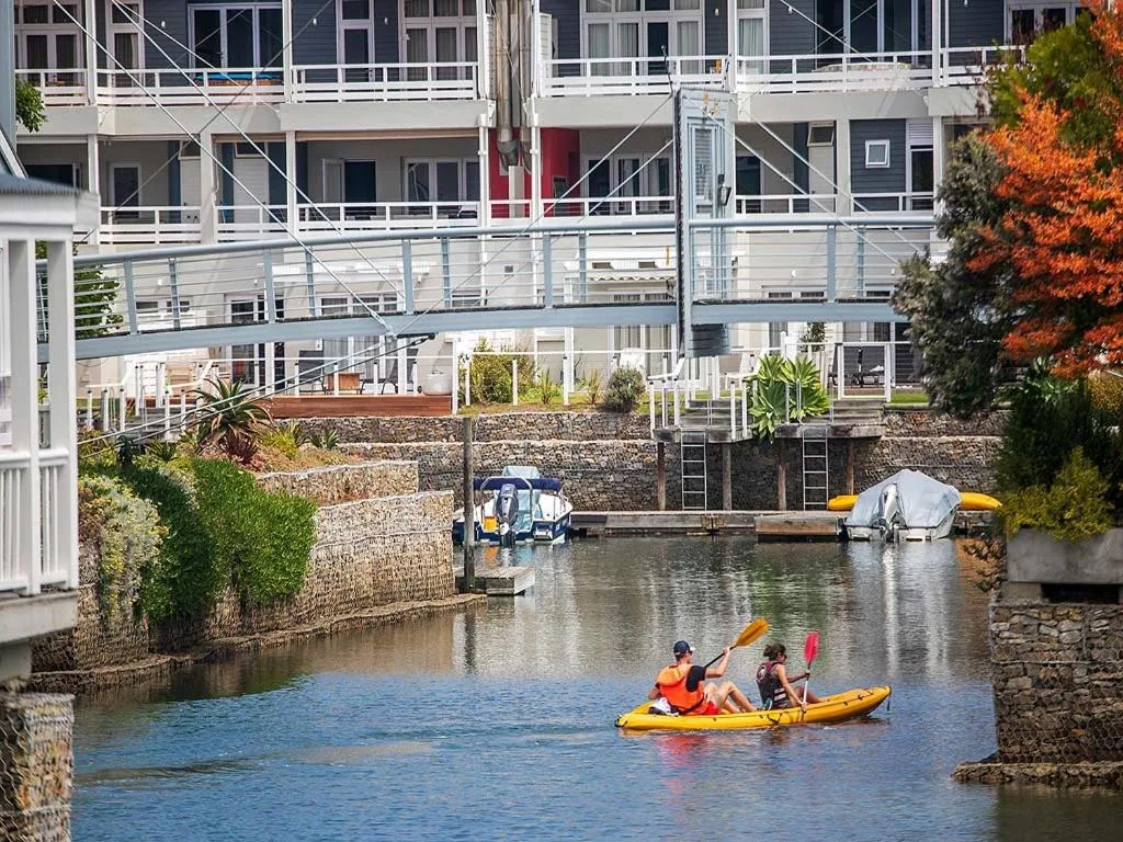 Waterfront view with kayakers on canal, modern architecture, autumn foliage