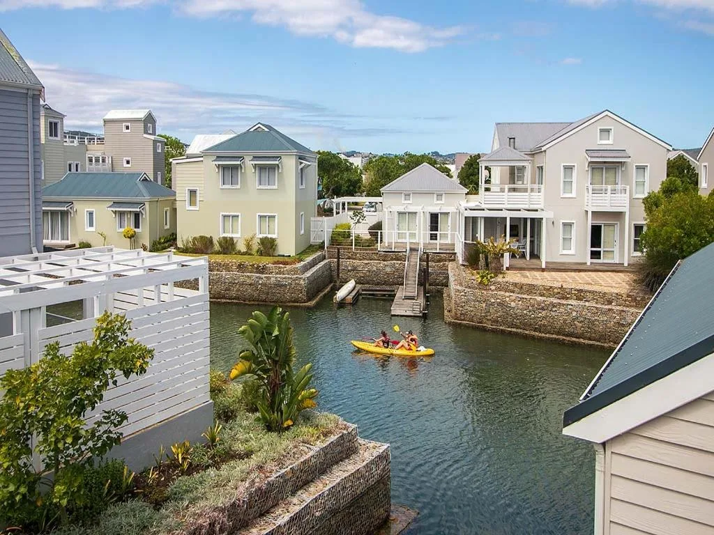 Waterfront canal with modern homes, kayaker, and moored boats under blue sky