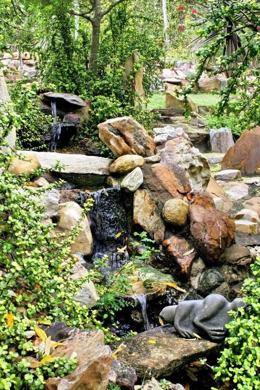 Natural stone water feature with flowing stream surrounded by lush green garden vegetation