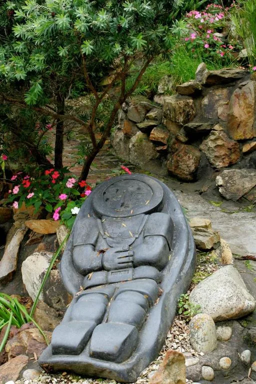Stone Buddha statue in lush garden with flowering plants and rocks