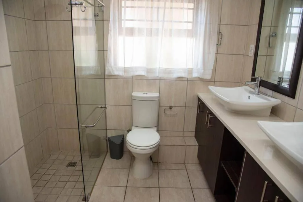 Spacious bathroom with double vanity, glass shower enclosure, and toilet