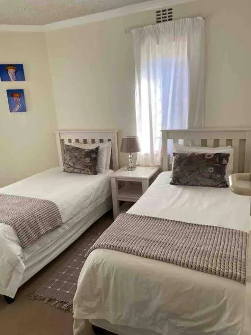 Twin bedroom with white beds, neutral decor, and bright natural light from windows