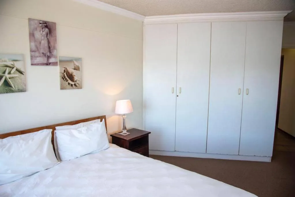 Spacious bedroom with queen bed, white wardrobe, and coastal wall art