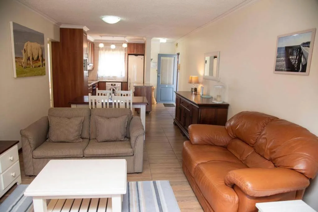 Open-plan lounge with beige armchair and cognac leather sofa, kitchen visible beyond