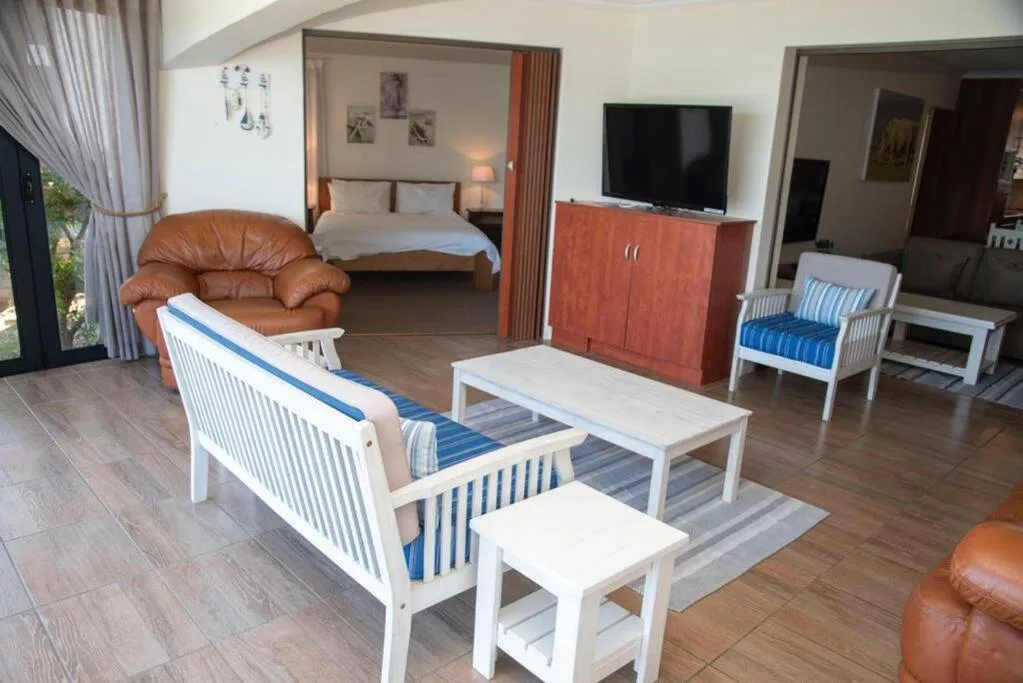 Open-plan lounge with white furniture, leather armchairs, and bedroom visible through doorway