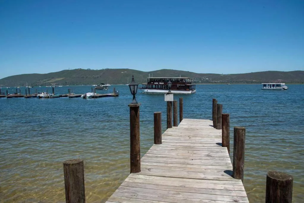 Wooden jetty extending into blue lagoon with boats and green hills beyond