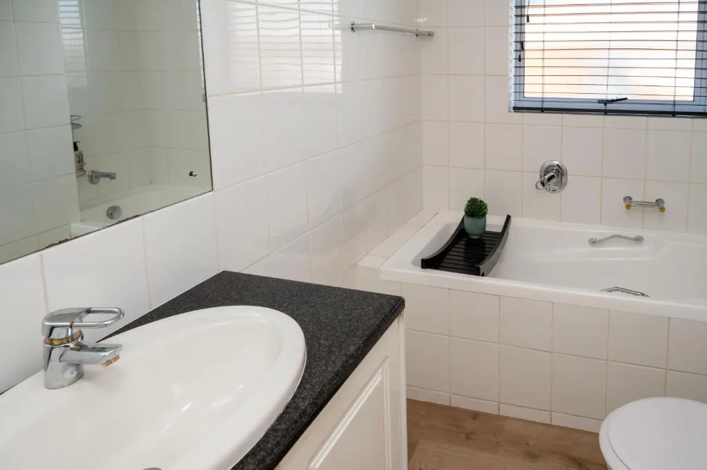 Clean white-tiled bathroom with vanity sink, bathtub, and toilet