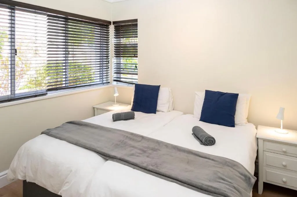 Bright bedroom with queen bed, navy pillows, and louvered windows overlooking garden