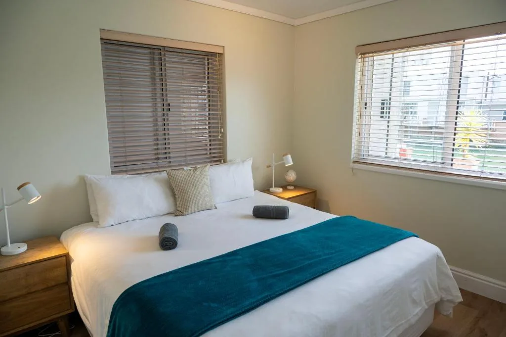 Bright bedroom with queen bed, white linens, teal runner, and shuttered windows