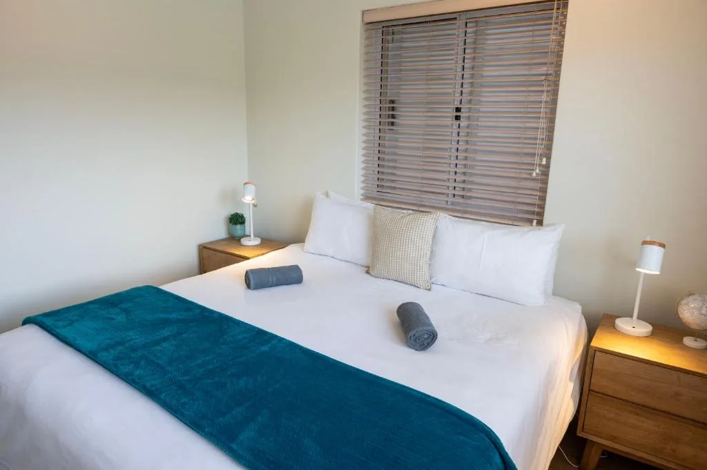Bright bedroom with queen bed, white linens, teal throw blanket, wooden nightstands