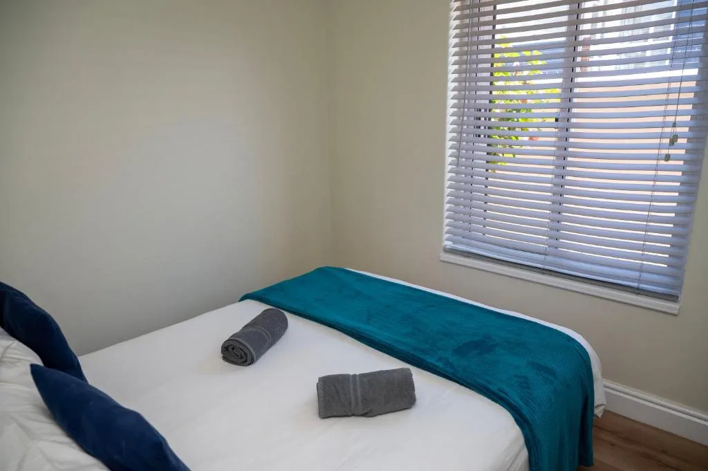 Bright bedroom with teal throw blanket and rolled towels on bed