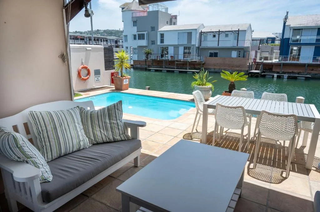 Waterfront deck with lounge seating, dining table, and swimming pool overlooking lagoon