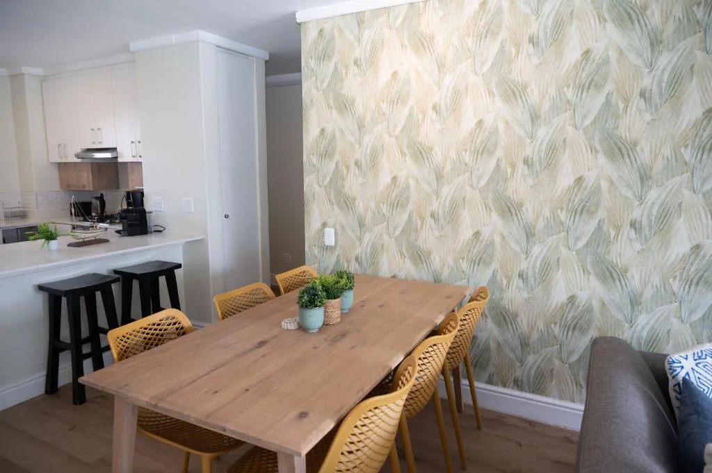 Wooden dining table with yellow chairs and leaf-patterned wallpaper backdrop