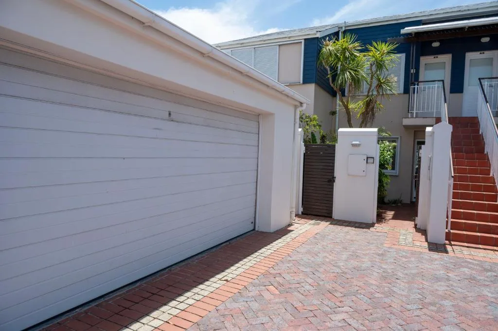 Modern townhouse entrance with white garage, brick paving, and tropical palm trees