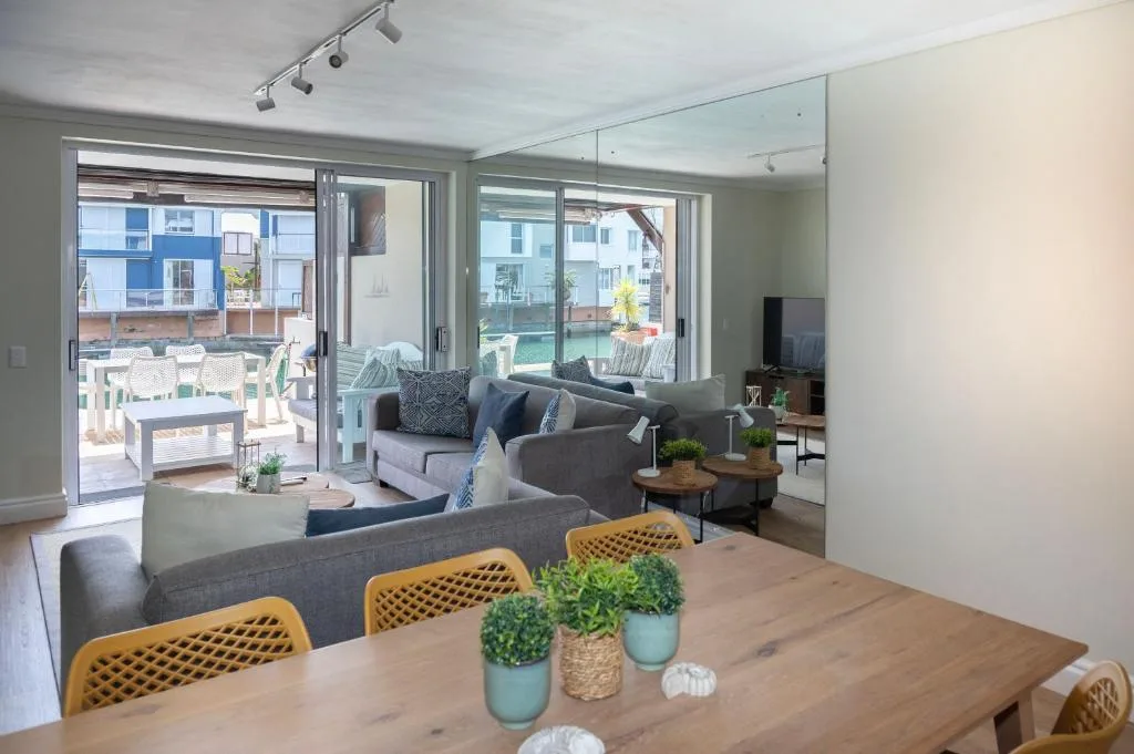 Open-plan living area with gray sofas, yellow chairs, and waterfront views through glass doors