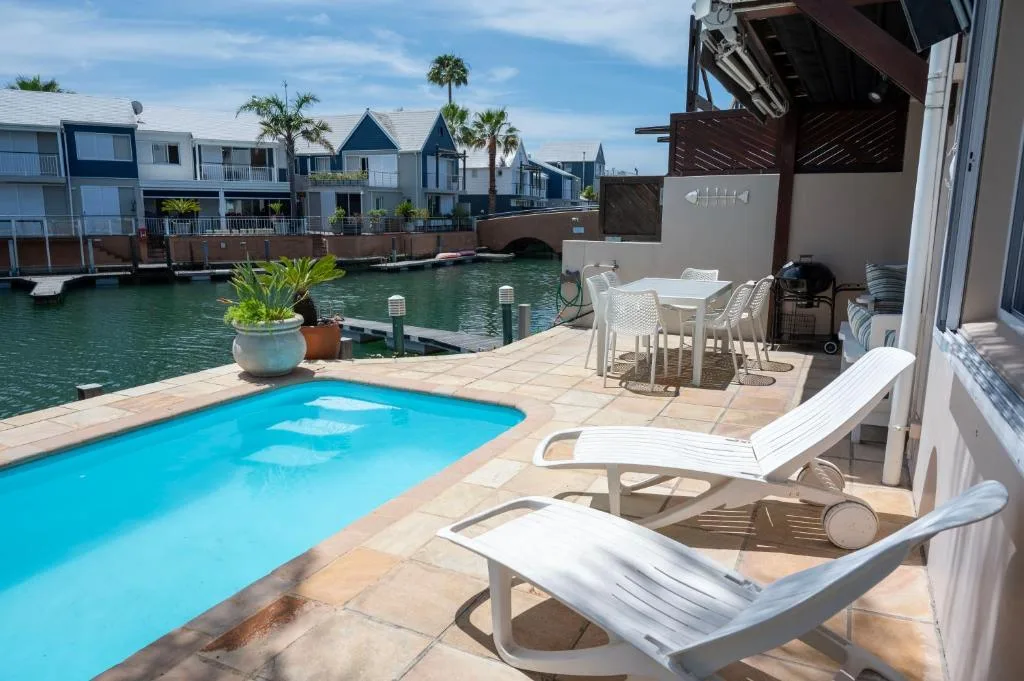 Bright blue swimming pool with loungers overlooking waterfront canal homes