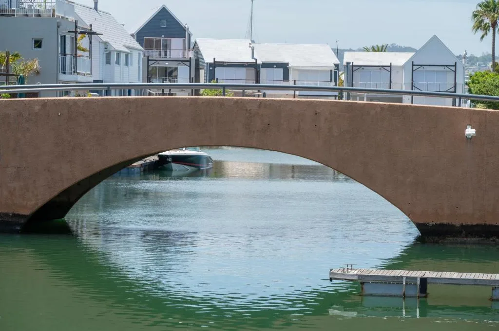Waterfront bridge and boathouses reflecting in calm lagoon waters