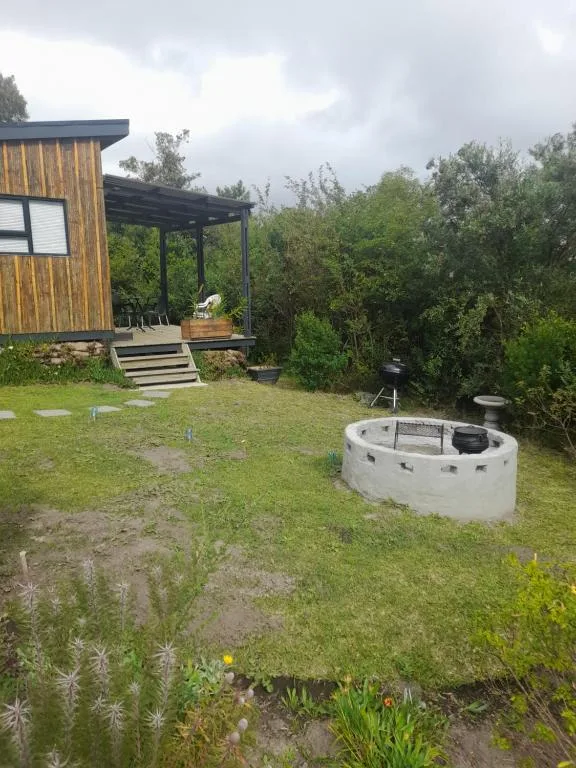 Modern cabin with wooden cladding, shaded deck, and circular fire pit in garden