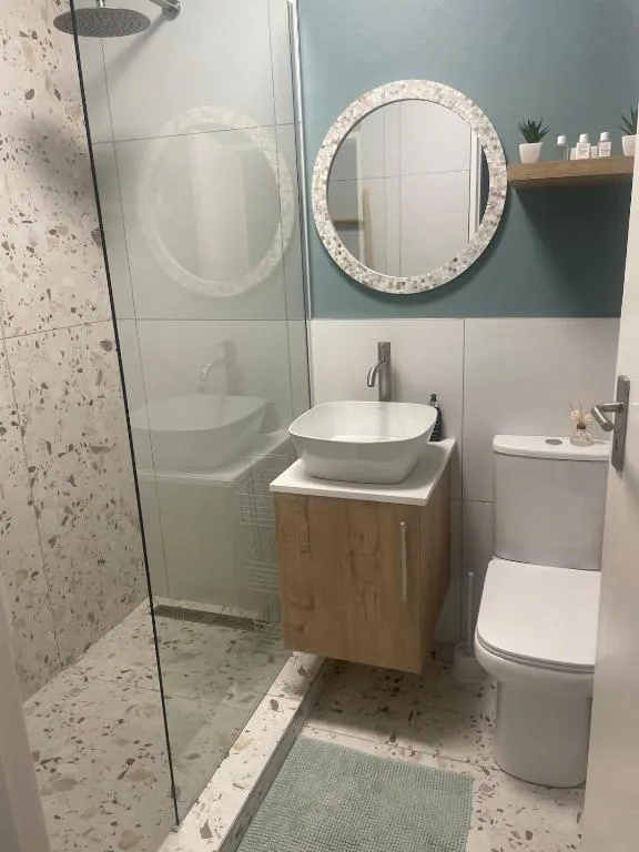 Modern bathroom with round mirror, vessel sink, wooden vanity, and walk-in shower