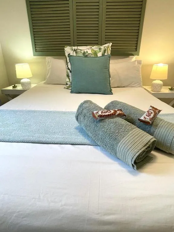 Neatly made bed with blue accents and welcome chocolates on towels