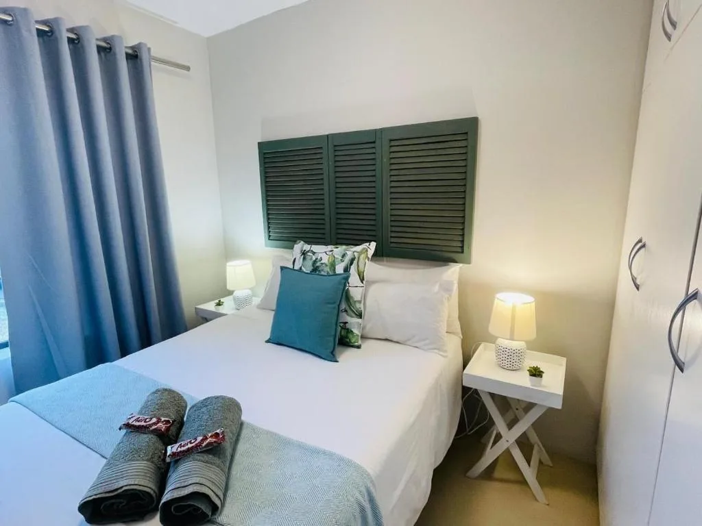 Bright bedroom with white bed, blue curtains, green louvre headboard art