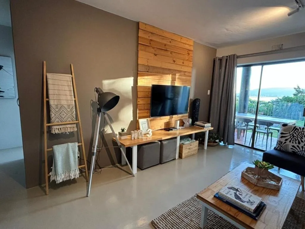 Modern living room with wooden TV unit, black sofa, and ocean view through glass doors