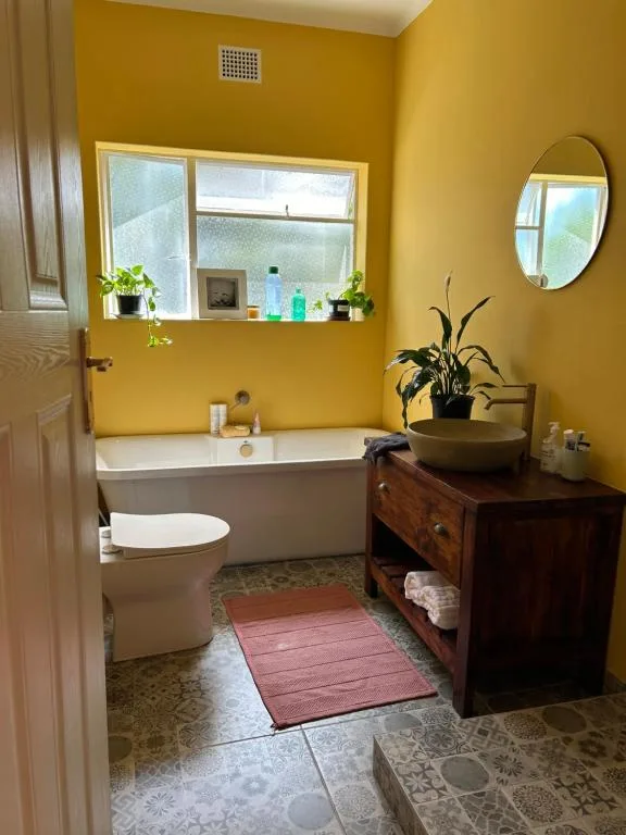 Bright yellow bathroom with bathtub, toilet, vanity and decorative plants