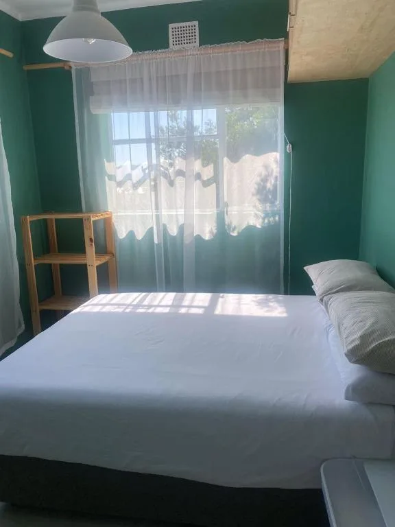 Bright bedroom with white bedding, green walls, sheer curtains, wooden shelf