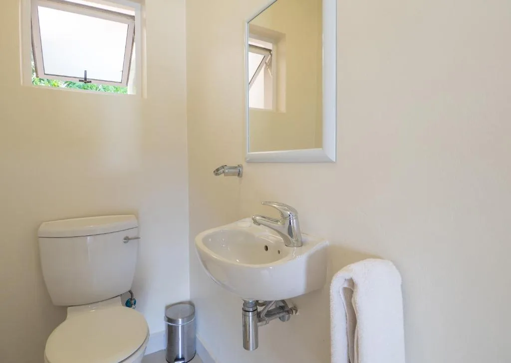 Clean bathroom with toilet, wall-mounted sink, and mirror with window