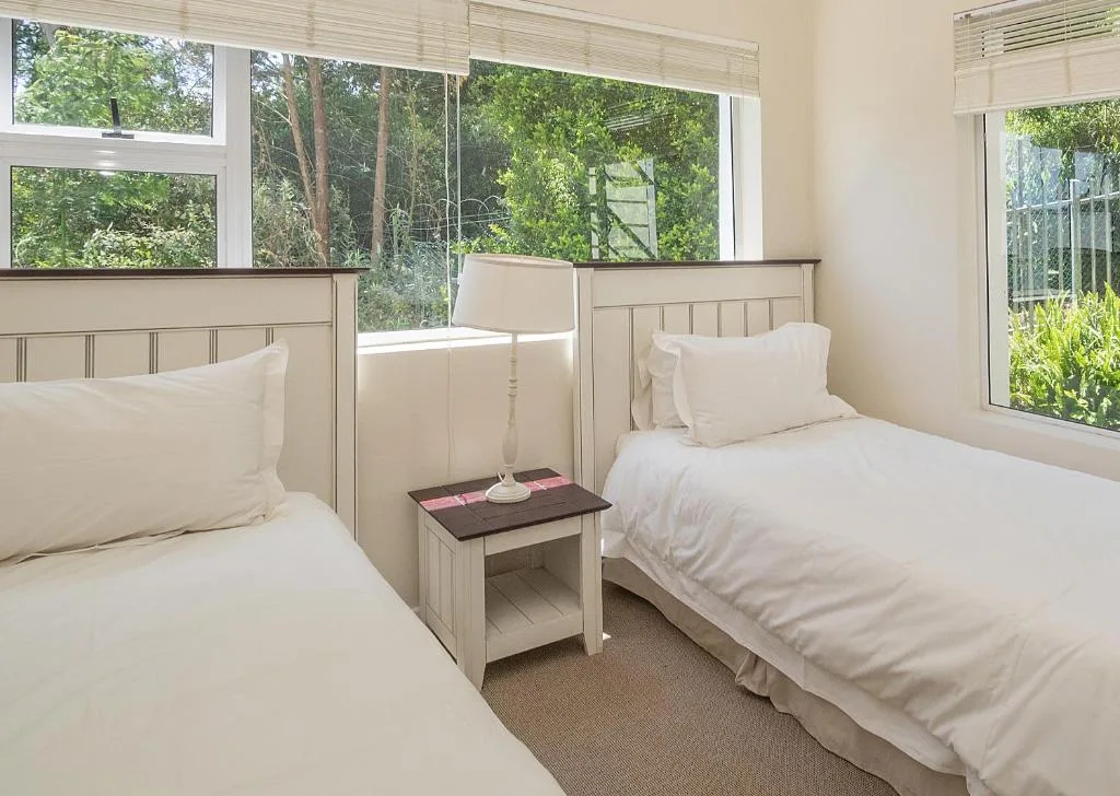 Bright twin bedroom with forest views through large windows and cream bedding