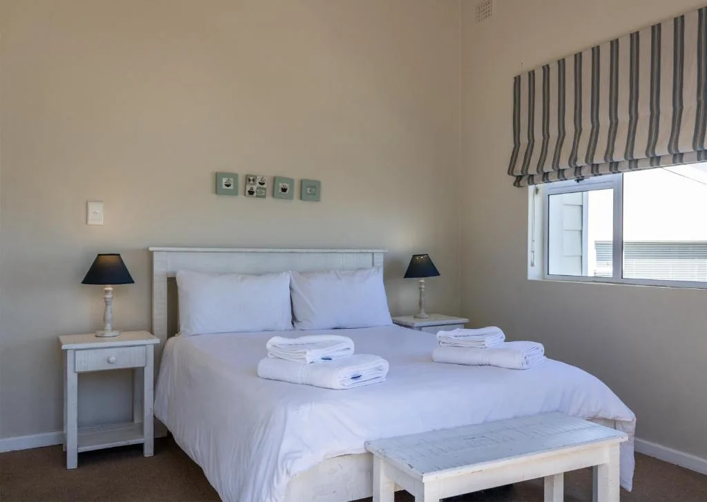 Bright bedroom with white bedding, fresh towels, and striped window blinds