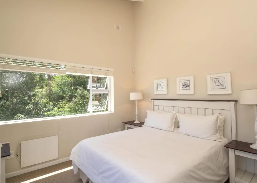 Bright bedroom with queen bed, white bedding, and large window overlooking trees