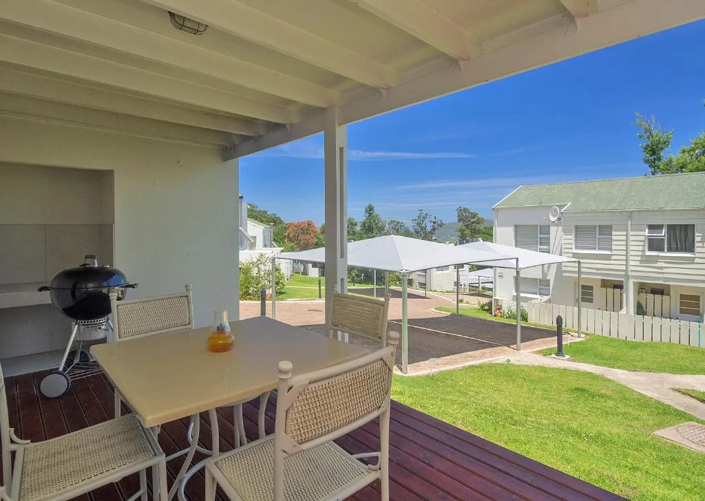 Covered patio with dining table, chairs, and braai grill overlooking gardens