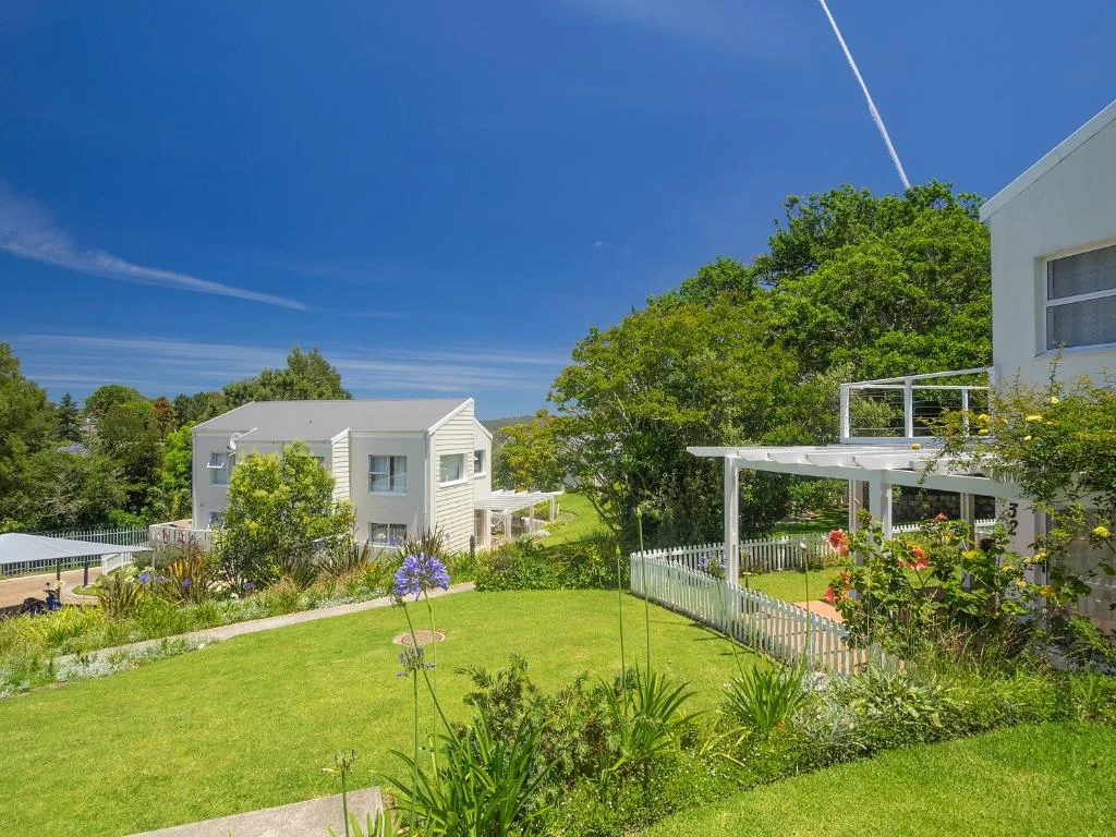 Modern white cottage with manicured gardens and pergola under blue sky