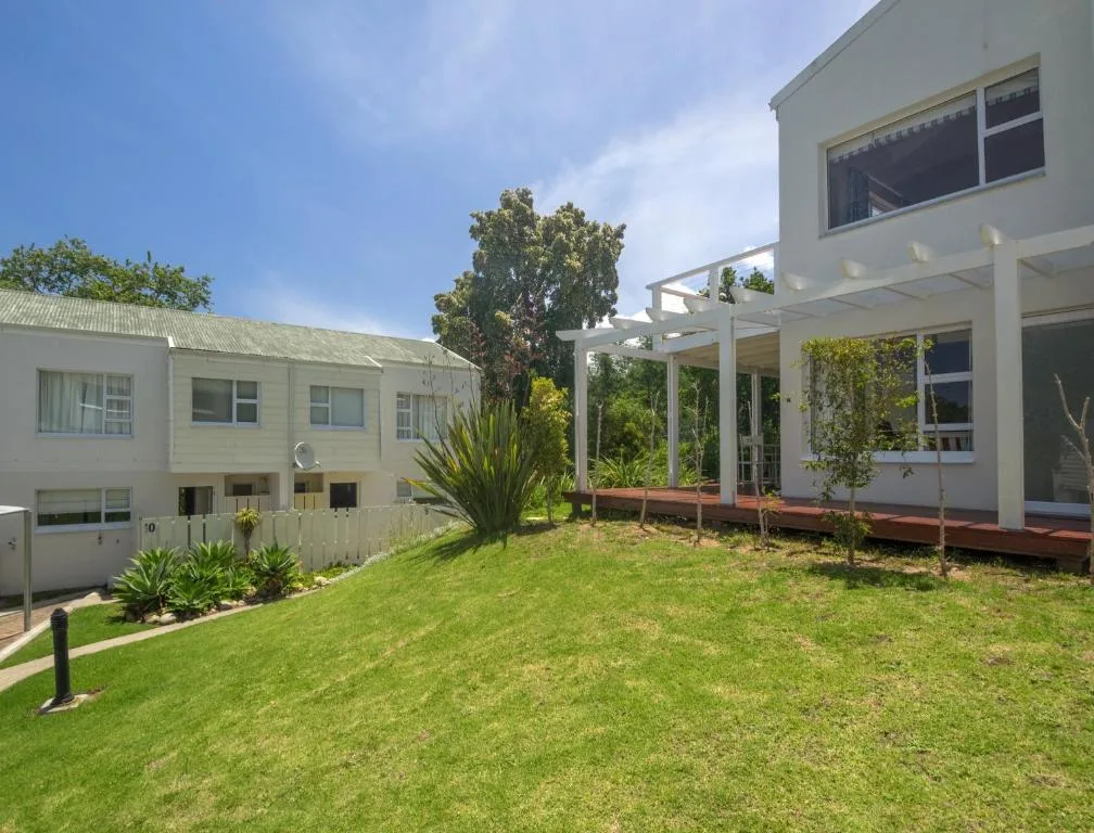 White modern holiday home with pergola deck and manicured garden lawn