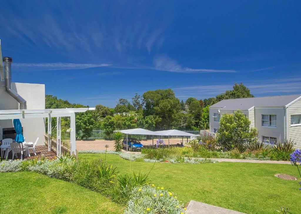 Modern white holiday home with manicured gardens and shaded outdoor seating area