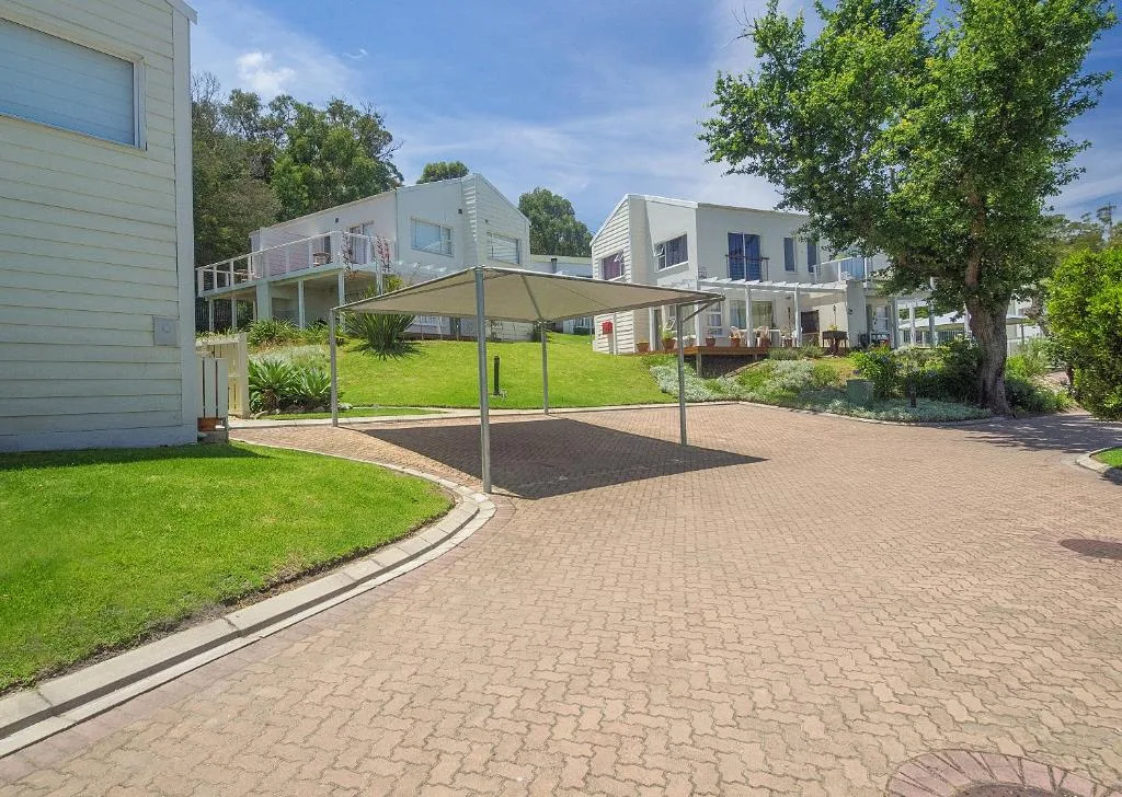 Modern white holiday home with manicured lawn, paved driveway, and shade structure
