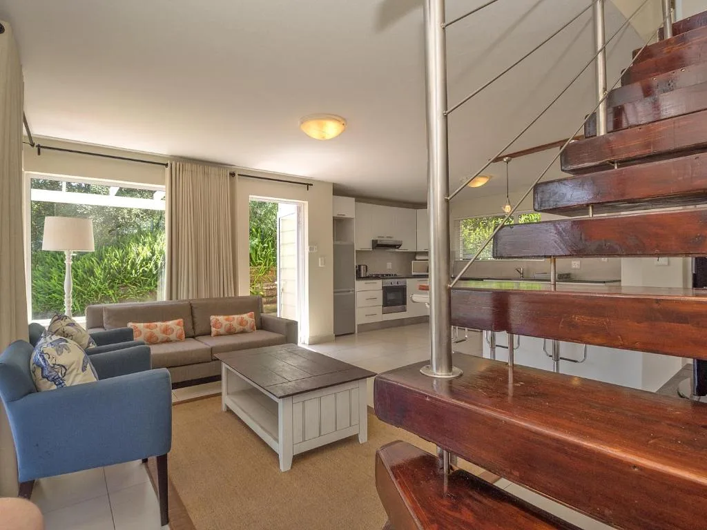 Modern living room with gray sofa, blue armchair, wooden stairs, and kitchen view