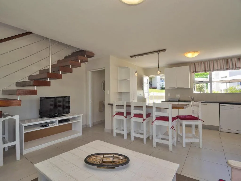 Open-plan lounge with TV, dining area, kitchen, and wooden staircase visible