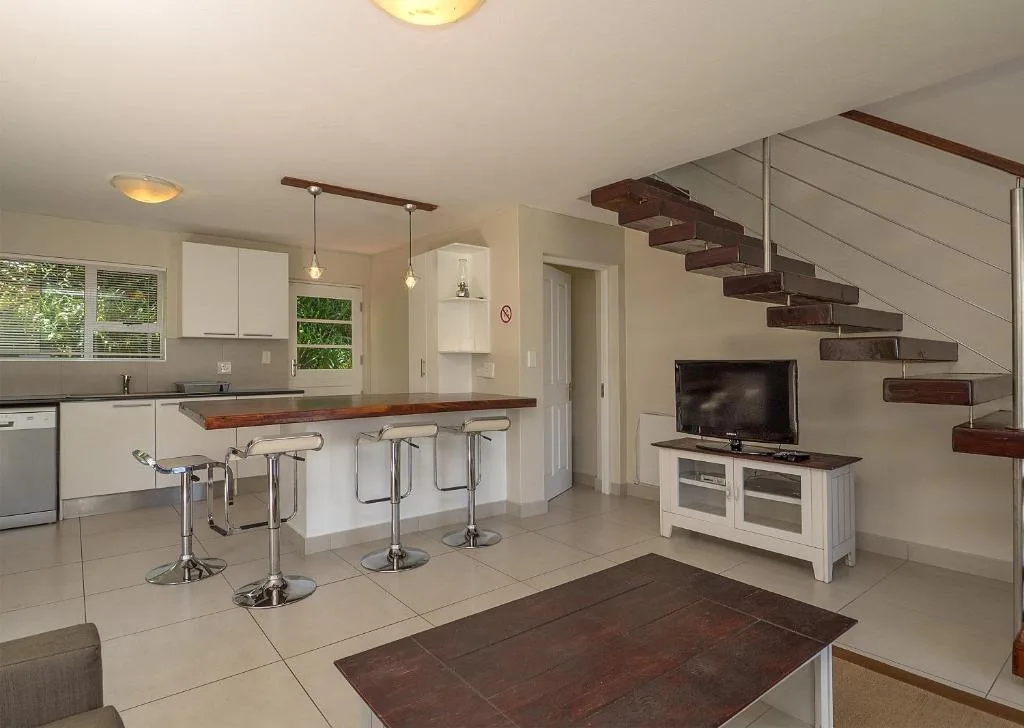 Open-plan lounge and kitchen with TV, bar seating, and wooden staircase