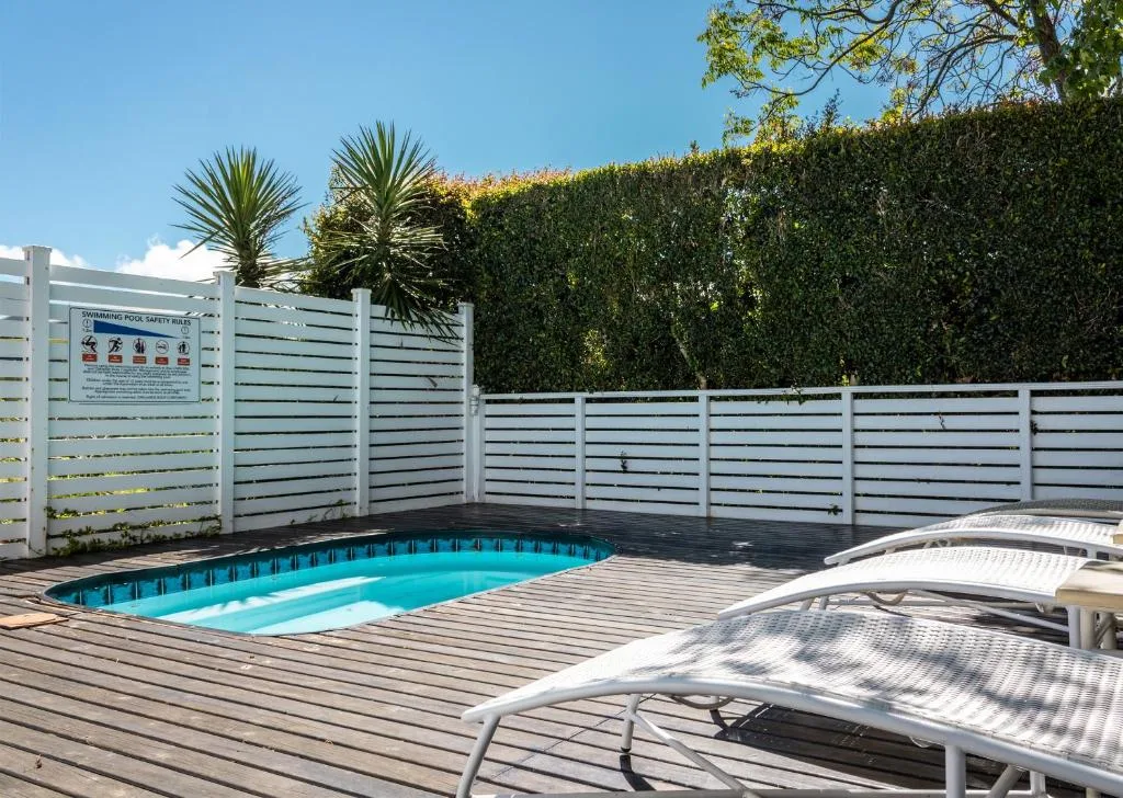 Turquoise swimming pool on wooden deck with lounge chairs and white fencing