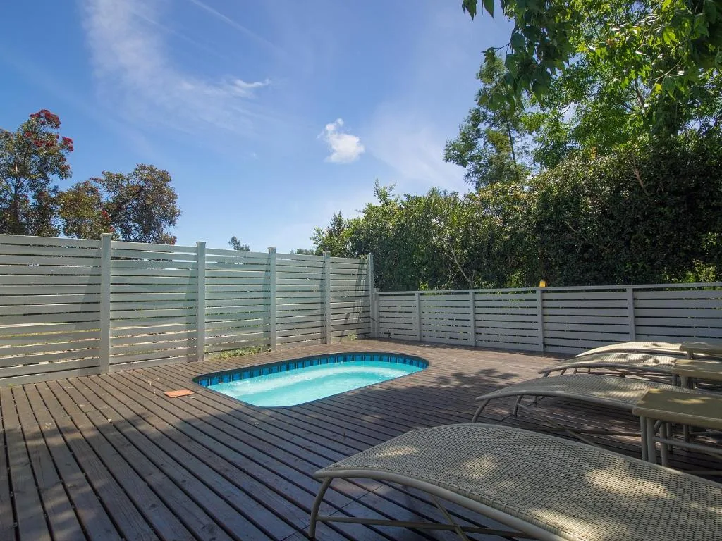 Small swimming pool on wooden deck with lounge chairs and fencing