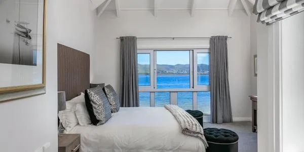 Bright bedroom with bed facing large windows overlooking blue water and mountains