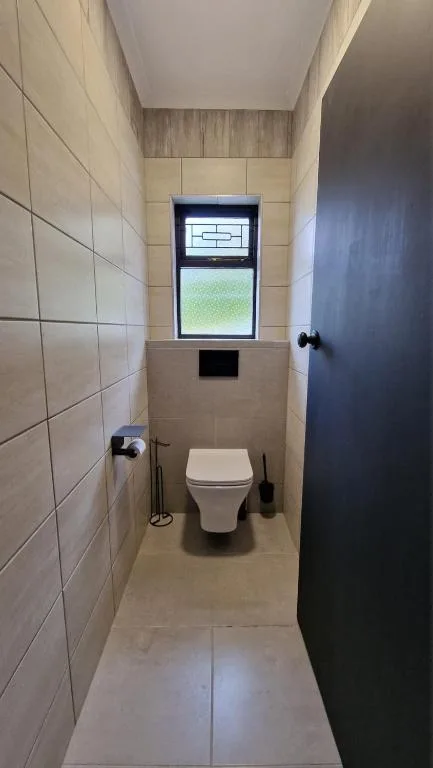 Modern toilet cubicle with tiled walls and window overlooking garden