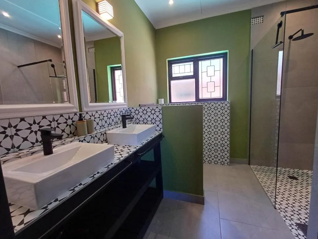 Modern bathroom with dual vanities, geometric tile work, green walls, and walk-in shower