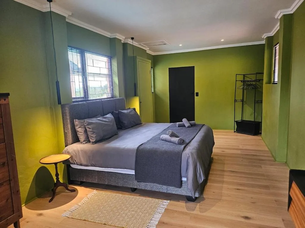 Spacious bedroom with queen bed, lime green walls, wooden flooring, and natural light