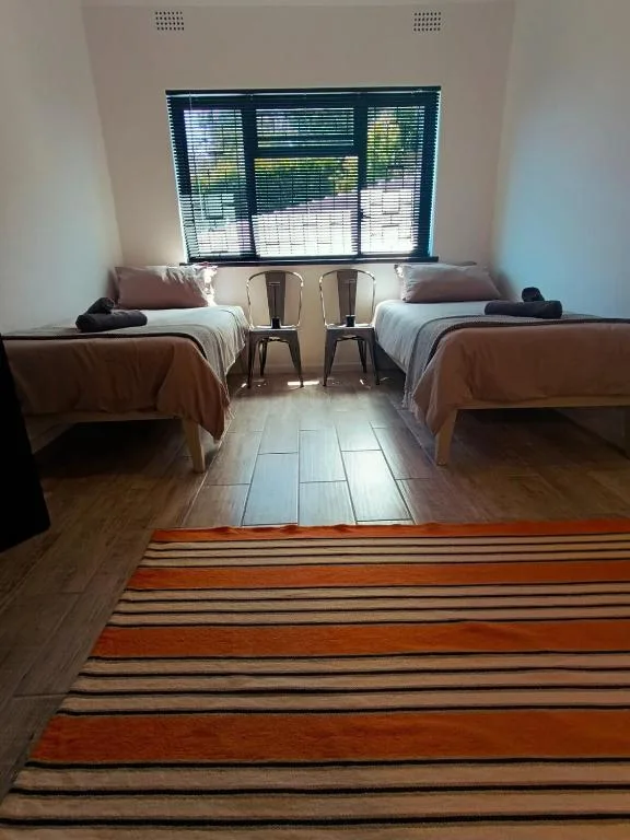 Twin bedroom with wooden beds, striped rug, and large window overlooking garden